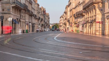 Günbatımında Bordeaux 'da L' Intendance Caddesi 'nde modern tramvaylar, bisikletler ve dükkanların ve kafelerin önünden geçen insanlar. Modern ve klasik mimariyi harmanlayan tarihi bir şehir manzarası. Fransa