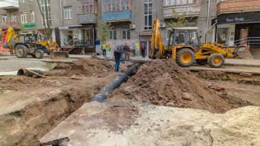 Kamu projeleri için su tedarik borusunun değiştirildiği boru hattı şantiyesinde çalışan kazıcı. Metal bir ipte boru kaldırma