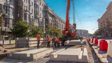 Yol inşaatı zamanına vinçle beton plakalar yerleştiriliyor. Şapkalı ve üniformalı endüstriyel işçiler. Şehir caddesindeki tramvay raylarının yeniden inşası. Mavi açık gökyüzü