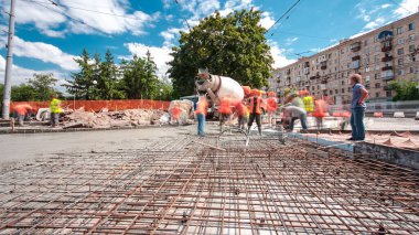 Tramvay rayları onarılan ve bakım süreleri yüksek olan yol inşaatı. Metal bir şebekeye beton dökülüyor. Kavşağın ortası. Arkaplanda yeşil ağaçlar