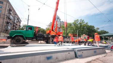 Beton plakaları yükleyip yüklüyorlar ve kamyondan blokları vinçle indiriyorlar. Tramvay rayları onarımı ve bakım süreleri olan yol inşaatı kavşağın orta kısmında hızlandırılmış..