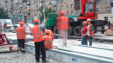 Tramvay rayları onarımı ve bakım zamanı olan bir yol inşaatı. Vinçle beton plakalar yerleştiriliyor. Kask ve üniformalı endüstriyel işçiler..