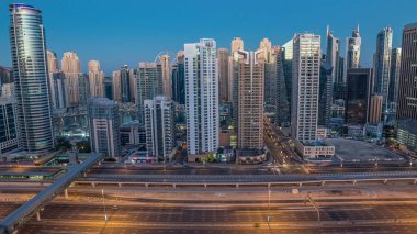 Dubai Marina gökdelenleri, güneş doğarken Dubai 'de JLT' den gündüz saatlerine kadar gökdelenler. Aydınlatılmış uzun gölgeli modern kuleler aşağı doğru ilerliyor ve Şeyh zayed yolunda trafik var..