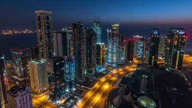 Katar 'ın Doha Zaman Çizelgesi' nde Batı Körfezi bölgesinin ufuk çizgisi. Aydınlatılmış modern gökdelenler. Gece güneş doğmadan çatıdan gökyüzü manzarası.