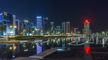 Geceleri Doha 'nın ufuk çizgisi. Yıldızlı gökyüzü Park Timelapse hiper hızından görünüyor, Katar. Aydınlatılmış gökdelenler ve kuleler çeşme suyuna yansıyor
