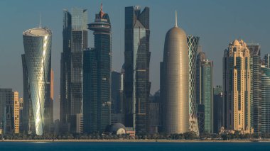 Katar 'ın Doha şehrinin ufuk çizgisi sabahın erken saatlerinde güneşin zengin ılık renkleri cam gökdelenlerden yansıyor..
