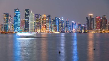 Doha şehir merkezi ufuk çizgisi günden geceye geçiş zamanı, Katar, Orta Doğu. Batı Körfezi 'ndeki aydınlık gökdelenler Körfez suyuna yansıyor. MIA parkından görüntü