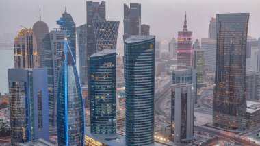 Batı Körfezi bölgesinin ufuk çizgisi Doha 'da günden geceye geçiş zamanı, Katar. Günbatımından sonra modern gökdelenlerin çatıdan görünüşü aydınlandı. Yolda trafik vardı.