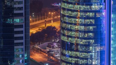 İçerideki cam ve çelik ofis aydınlatması ve çalışan insanların çok katlı binasının zaman çizelgesi. Gökdelenlerin gece aydınlanması. Yollarda trafik vardı. Doha, Katar