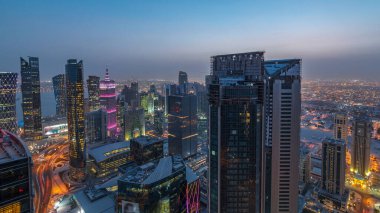 Batı Körfezi bölgesinin ufuk çizgisi Doha 'da günden geceye geçiş zamanı, Katar. Günbatımından sonra modern gökdelenlerin çatıdan görünüşü aydınlandı. Yolda trafik vardı.