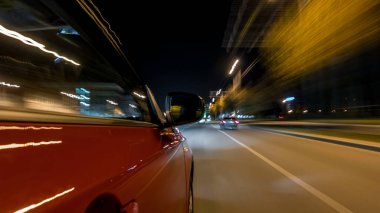 Hızlı arabanın yanından gelen bir drivelapse, gece caddesinde hızla ilerliyor. Işıklar yüksek hızda arabayı yansıtıyor. Modern bir şehrin hızlı ritmi. Bulanık hareket