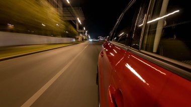 Hızlı arabanın yanından gelen bir drivelapse, gece caddesinde hızla ilerliyor. Işıklar yüksek hızda arabayı yansıtıyor. Modern bir şehrin hızlı ritmi. Bulanık hareket