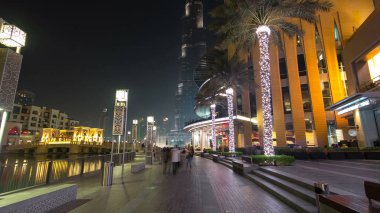 Dubai, BAE 'de çeşmenin yanında yürüyüş alanı var. İnsan yapımı gölde aydınlatılmış palmiyeler ve sokak lambaları