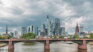 Frankfurt 'un, ana nehir ve Ignatz Bubis Köprüsü' yle olan hiperhızlandırılmış silueti. Gökdelenler ve kilise kuleleri dramatik bulutların altındaki suya yansıyor. Frankfurt, Almanya