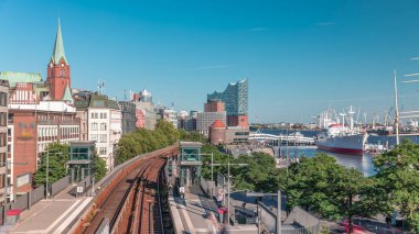 Almanya 'nın Hamburg kentindeki Landungsbrucken istasyonuna gelen trenler son sürat ilerliyor. Metroya binen insanlar mavi gökyüzünün altında Elbphilharmonie, liman ve marina ile panoramik manzara