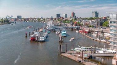 Almanya 'nın Hamburg kentinde Elbe nehir kenarının hava zaman çizelgesi. Rıhtımın yakınındaki Jan Fedder Gezinti Güvertesi, marina ve geçen gemilerle sahile manzara. Elbe Nehri kıyısındaki canlı şehir manzarası