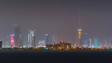 Gökdelenler ve Kuveyt 'teki Kurtuluş Kulesi' nin zaman çizelgesi alacakaranlıkta aydınlandı. Deniz manzaralı, sisli havada suda yansıyan. Kuveyt Şehri, Orta Doğu.