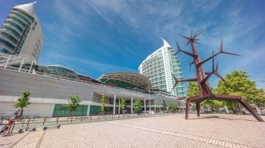 Vasco da Gama Alışveriş Merkezi 'ne girip çıkan ziyaretçiler, arka planda modern kuleler ve Homem-Sol (Sun-Man) heykelleri. Parque das Nacoes bölgesi. Lizbon, Portekiz