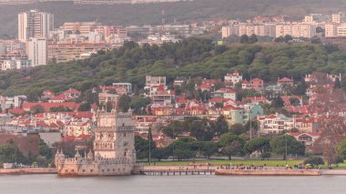 Portekiz 'in Lizbon kentindeki Belem Kulesi' nin havadan görünüşü, Tagus Nehri kıyısındaki ünlü UNESCO simgesi. Sahilde ve yemyeşil parkta gezinen insanların büyüleyici günbatımı sahnesi, tarihi ve güzelliği harmanlıyor.
