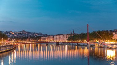 Lyon 'daki Saone Nehri' nin üzerindeki Palais du Justice Köprüsü 'nde, günden geceye geçiş. Rıhtımdaki aydınlık binalar gün batımından sonra suya yansıyor.