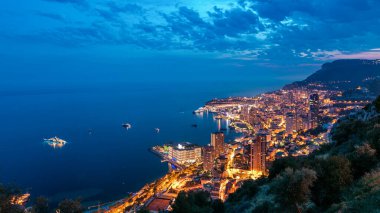 Monako 'nun havadan panoramik manzarası. Büyük Corniche yolundan geceye geçiş zamanı, Monako France. Akşam aydınlatması. Limanın suyundaki yansımalar