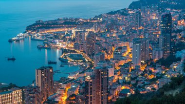 Monako 'nun büyük Corniche yolundan gece geçiş zamanına, Monako Fransa' ya giden hava manzarası. Akşam aydınlatması. Limanın suyundaki yansımalar