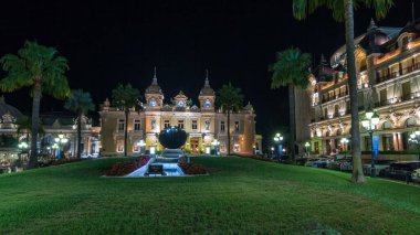 Monte Carlo 'da Grand Casino' yla birlikte Monaco 'da gece hiperhızlandırılmış zaman dilimi. Çevrede tarihi aydınlık binalar var. Tepedeki saat. Avuçlar yana..