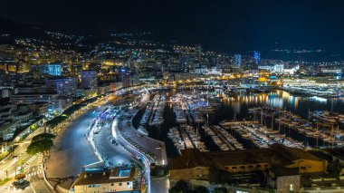 Monte Carlo 'nun Panorama' sı geceleyin Herkül Limanı ile Monako köyündeki gözlem güvertesinden hızla yükseliyor. Liman manzaralı, aydınlık binalar ve yatlar. Yolda trafik vardı.