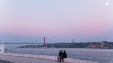 Gün batımında Tagus nehri üzerindeki 25. Köprü ay ışığı altında Belem Kulesi, Lizbon ve Portekiz yakınlarındaki sahil manzaralı.