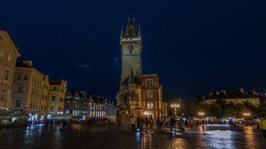 Prag Eski Belediye Binası 'nda gece vakti hızlandırılmış. Tanınmayan turistler yürüyor. Aydınlatılmış kulesi olan eski kasaba meydanı