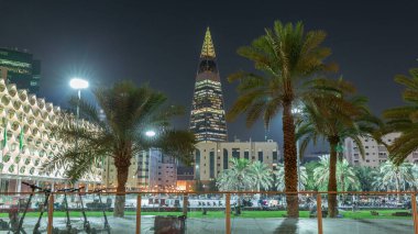 Kral Fahad Ulusal Kütüphanesi 'nin avuçlar ve parlayan kuleyle aydınlatılmış cephesinin perspektif gece zaman çizelgesi. Suudi Arabistan 'ın Riyad şehrinde insanlar canlı meydanda yürüyorlar..