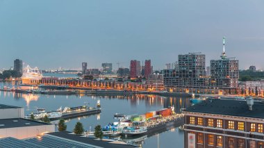 Güneş doğmadan önce Maashaven 'daki kuleler üzerindeki hava manzarası demirli gemilerle, Katendrecht ve Maas Nehri' yle, Rotterdam 'la geçiş zamanlarını gösteriyor. Aydınlatılmış fabrika ofis ve olay alanına dönüştürüldü