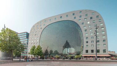 Rotterdamse Markthal 'ın dış yüzeyinde aşırı kayma. Dükkanları ve restoranları olan ikonik at nalı şeklinde bir bina. Meydanda gezinen insanlar. Gökdelenler ve arka planda canlı bir şehir manzarası