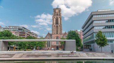 Laurenskerk 'in (Saint Lawrence Kilisesi) Grotekerkplein, Rotterdam' daki hiperlapesi. İnsanlar mavi bulutlu gökyüzünün altında çimlerde dinleniyorlar. Kanal merdivenlerinin yanında saati olan tarihi çan kulesi. Hollanda