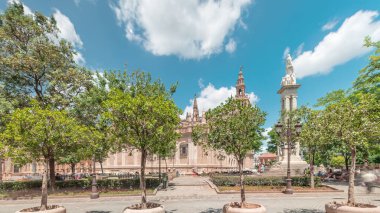 Plaza del Triunfo zaman atlaması ve Sevilla Katedrali 'nin kusursuz gebelik anıtı. Yeşil ağaçlar, tarihi mimari, bulutlu mavi gökyüzü. Endülüs, İspanya 'da manzara