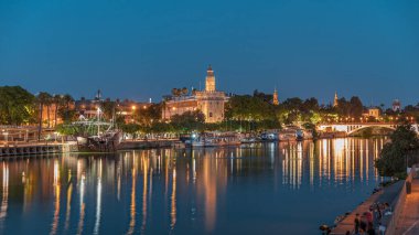İspanya, Sevilla 'daki Torre del Oro gözlem kulesi. Günbegün geçiş zamanı, şehrin ışıkları su ve deniz manzarasını yansıtıyor. Guadalquivir Nehri boyunca yüzen bir tekne.