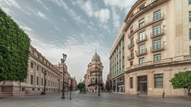 Avda boyunca yürüyen yayalar. De la Constitucion, Seville, İspanya 'nın Casco Antiguo bölgesindeki ana cadde. Edificio de la Adriatica ile zaman atlaması, tarihi binalar ve geçen tramvaylar