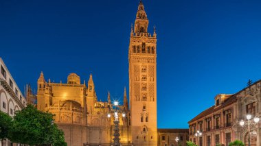 La Giralda ve Seville Katedrali günden geceye geçiş zamanı, gün batımından sonra altın ışıklarla parıldıyor. Tarihi çan kulesi, gotik detaylar ve Seville, İspanya 'da aydınlatılmış sokaklar.