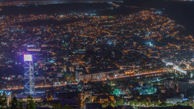 Gürcistan 'ın gökdelenleri, işlek bulvarda yer alan Tiflis hava zaman çizelgesinde aydınlatılmış cam kule. Tarihi bina ve nehir. Bakış açısından bak