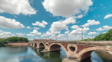 Toulouse, Fransa 'da Garonne Nehri ve Pont Neuf zaman aşımına uğradı. Bu Rönesans kemer köprüsü bulutlu mavi gökyüzünün altındaki suya yansıyor. Yeşil ağaçlı rıhtım