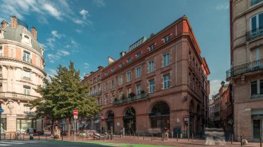 Toulouse, Occitanie, Fransa 'da Rue de Metz' in zaman çizelgesini gösteren panorama, tarihi cepheleri, dükkanları, kafeleri, trafiği ve mavi bulutlu gökyüzünü gösteriyor. Şehrin göbeğinde canlı bir şehir manzarası