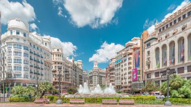 Valencia, İspanya 'da Belediye Meydanı' ndaki (Plaza del Ayuntamiento Meydanı) zaman atlaması. Büyük mimari, çiçek açan yeşillik ve bulutlu bir gökyüzünün altında su jetleri. İnsanlar canlı meydanda geziniyor..
