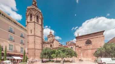 Valencia, İspanya 'da Plaza de la Reina' nın panoramik zaman atlaması. Tarihi bir kilise kulesi, hareketli kafeler ve sıcak Akdeniz mavi bulutlu gökyüzünün altında merkezi bir çeşme ile dolu canlı bir meydan..
