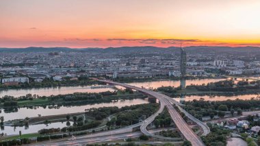 Viyana üzerinde gökdelenler, karayolu kavşağı ve Avusturya 'daki nehir kenarından geceye geçiş yapan hava panoramik manzarası. Akşam üstü Tuna Kulesi 'nden gün batımından sonra gökyüzü