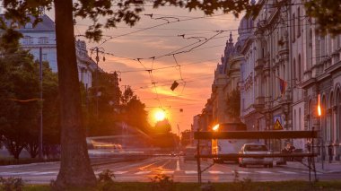 Street with sunset in the Croatian capital Zagreb. People sitting on the bench near tree. Road traffic and tram rails