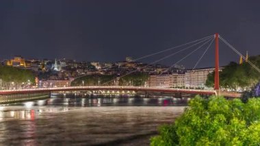 Saone Nehri üzerindeki kırmızı asma köprü ile Lyons şehir manzarasının gece zaman çizelgesi, aydınlatılmış kıyı şeridi gece boyunca suya yansıdı. Fransa