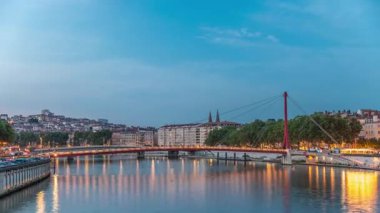 Lyon 'daki Saone Nehri' nin üzerindeki Palais du Justice Köprüsü 'nde, günden geceye geçiş. Rıhtımdaki aydınlık binalar gün batımından sonra suya yansıyor.