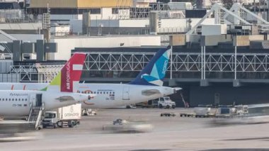 Lizbon Havaalanı Humberto Delgado saatine park etmiş uçaklar hareket ediyor. Pist aktivitesi, terminaller, şehir silueti ve açık bir gökyüzü altında hareket halindeki farklı havayolu şirketlerinin uçakları. Lizbon, Portekiz.
