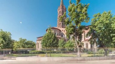 Fransa 'nın Toulouse kentindeki Saint Sernin Bazilikası' nın kaldırımlı parvisleri. Zaman atlaması. Avrupa 'nın en büyük Roma kilisesi tuğla çan kulesi, kemerli kapılar, yeşil ağaçlar ve mavi gökyüzü.