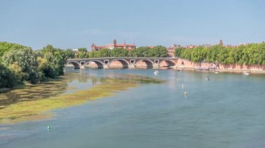 Toulouse, Fransa 'da Garonne River ve Pont Neuf saatleri. Rönesans kemer köprüsü mavi gökyüzünün altındaki suya Daurade Leydisi Bazilikası ile yansıyor. Yeşil ağaçlı rıhtım